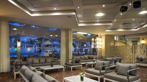 Un'accogliente hall d'hotel moderna con diverse zone relax, ampie finestre e una parete decorativa.