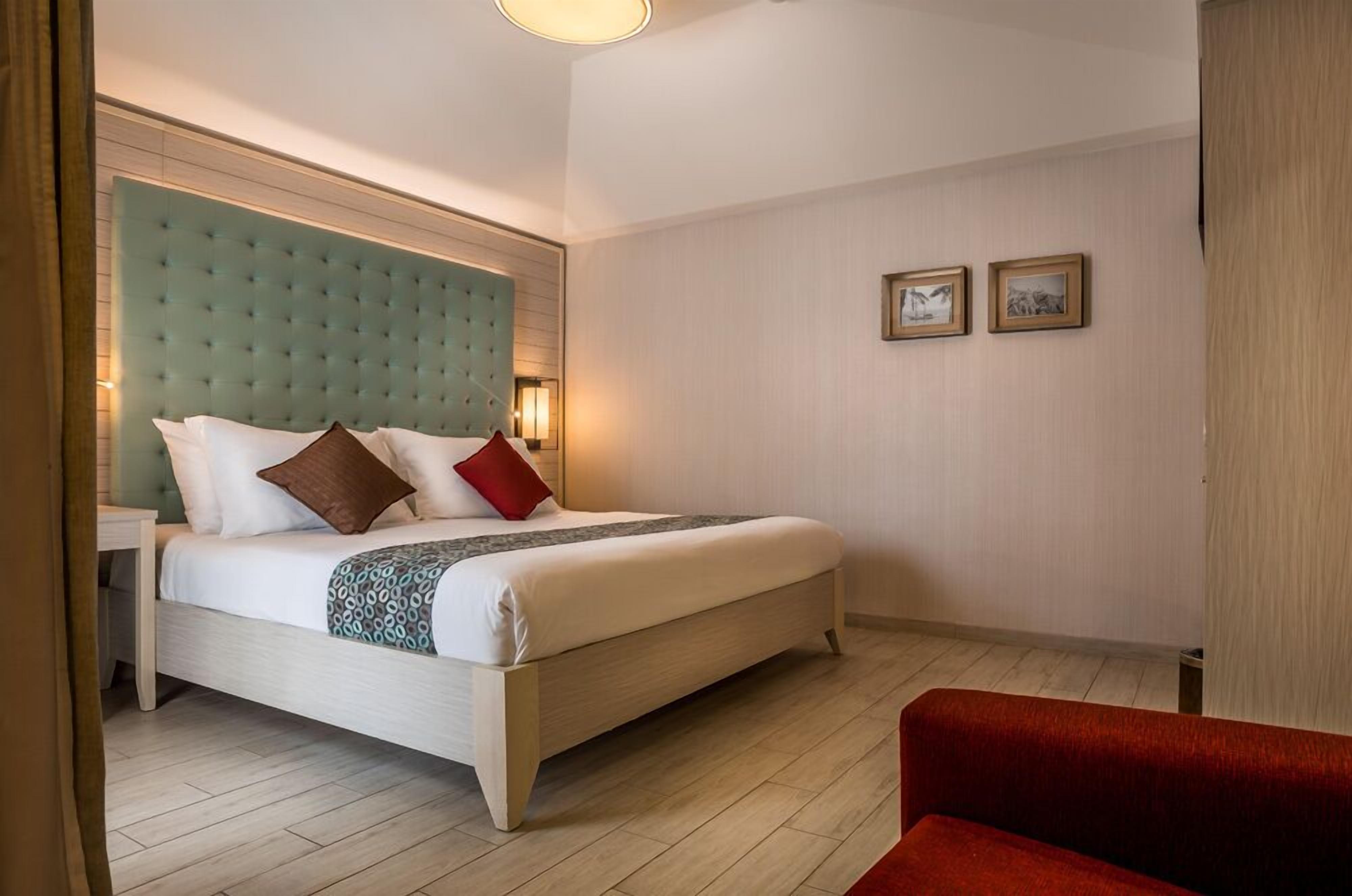 Quarto de hotel com uma cama grande, uma poltrona vermelha e duas fotografias emolduradas na parede.
