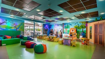 A children's play area with colorful furniture, a mural, and a view of the outdoors.