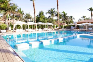 Una piscina con sillas de descanso y sombrillas, rodeada de palmeras.