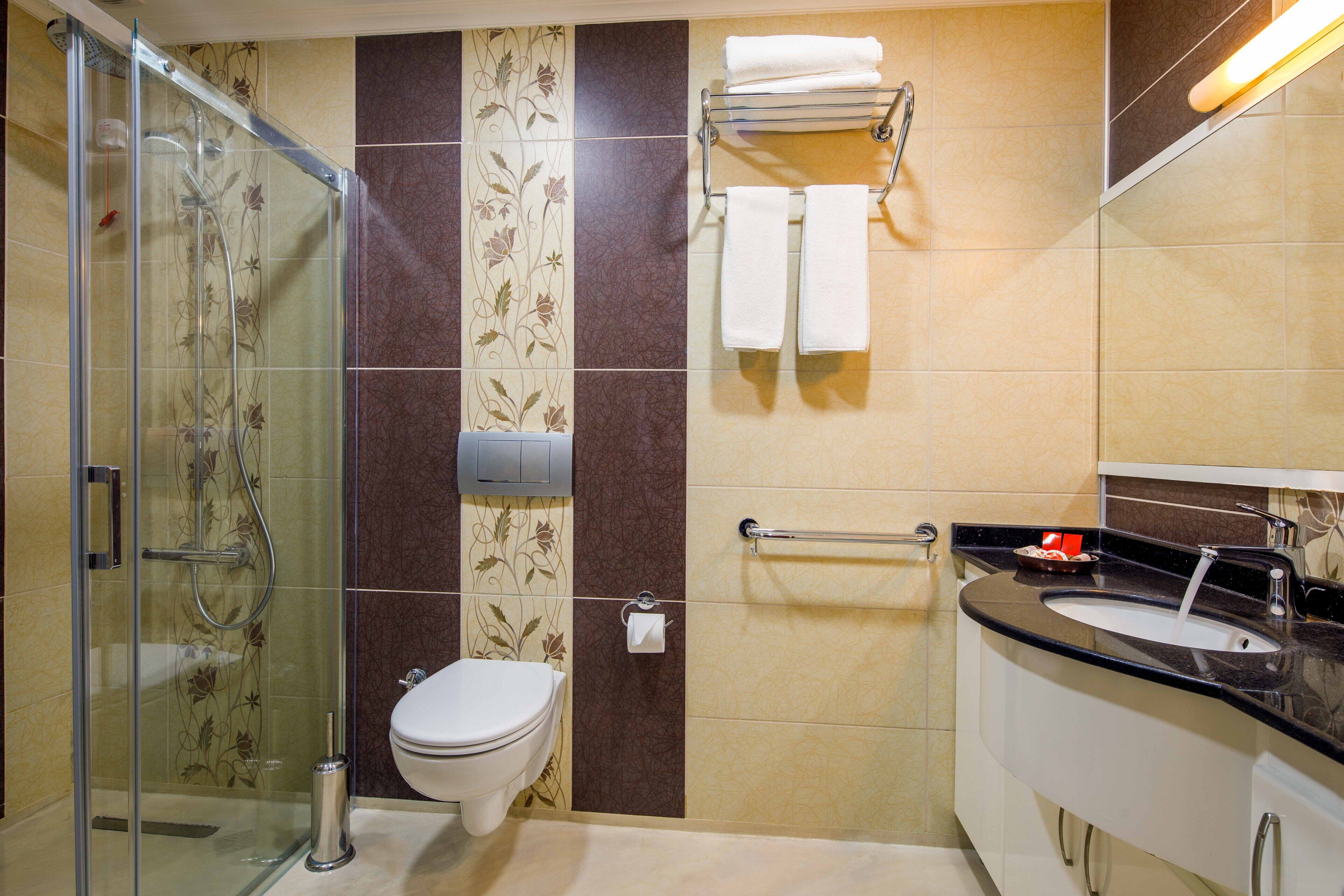 Un baño con cabina de ducha de vidrio, inodoro, lavabo con espejo y perchero para toallas.