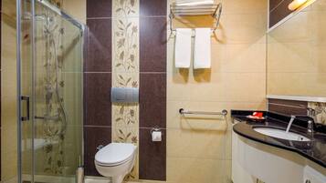 Un baño con cabina de ducha de vidrio, inodoro, lavabo con espejo y perchero para toallas.