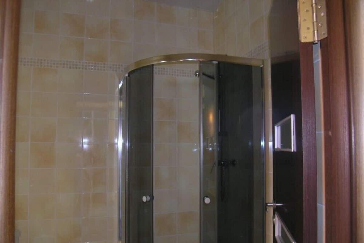 A glass-enclosed shower stall with a curved door, tiled walls, and a visible shower control panel.