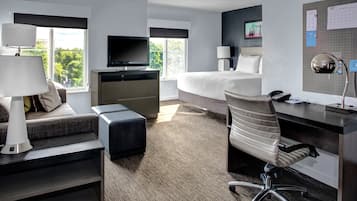 A hotel room with a bed, desk, chair, TV, and lamp.