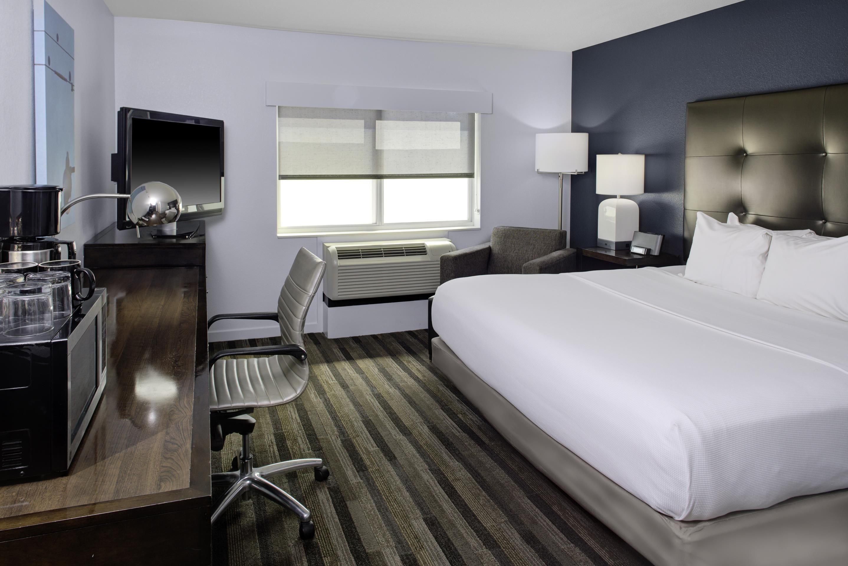 A hotel room with a bed, desk, chair, and a window with blinds.