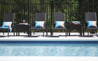 Un área junto a la piscina con cuatro sillones de mimbre, cada uno con cojín.