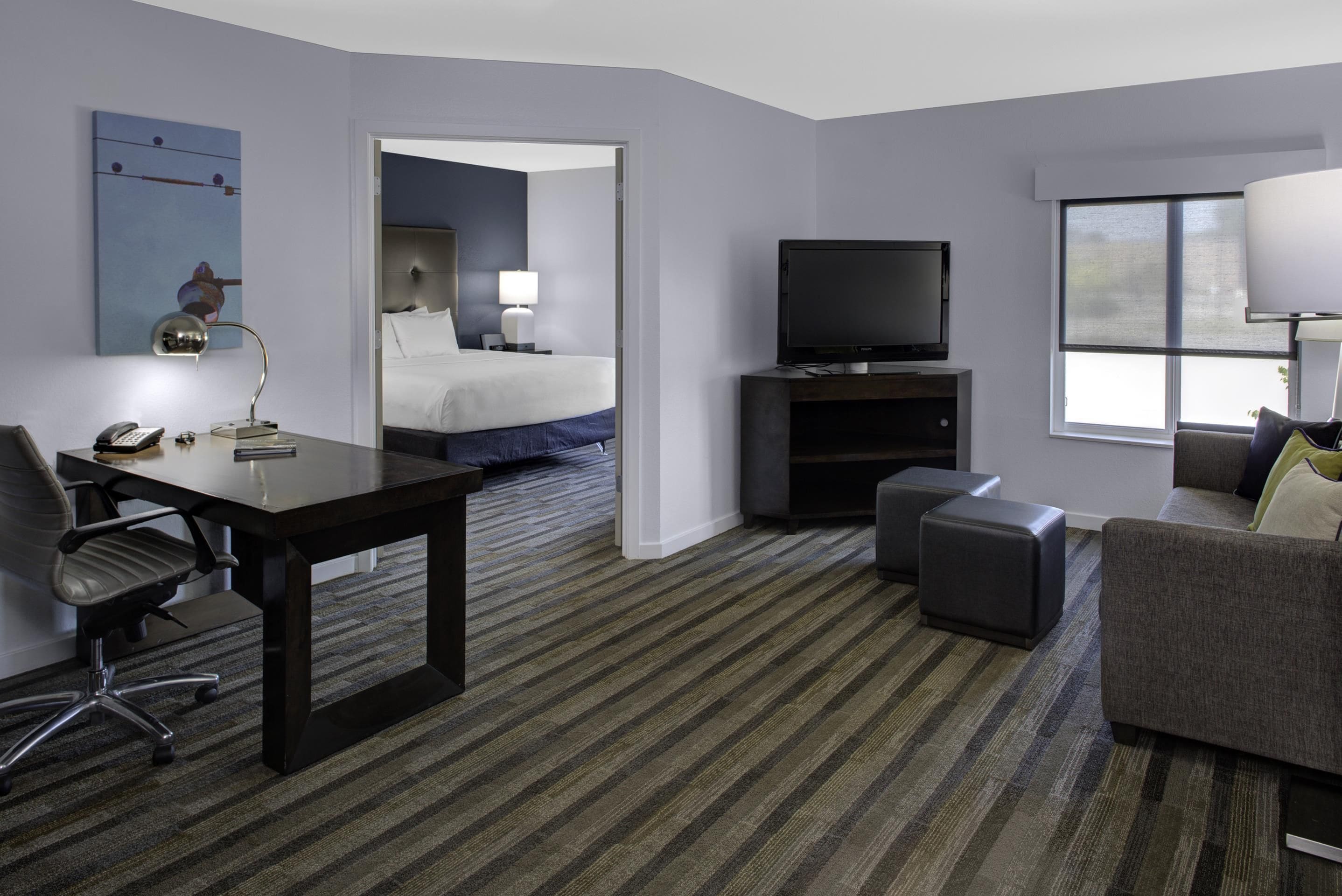 Ein Hotelzimmer mit einem Bett, einem Schreibtisch mit Telefon, einem Fernseher und einem Sofa.