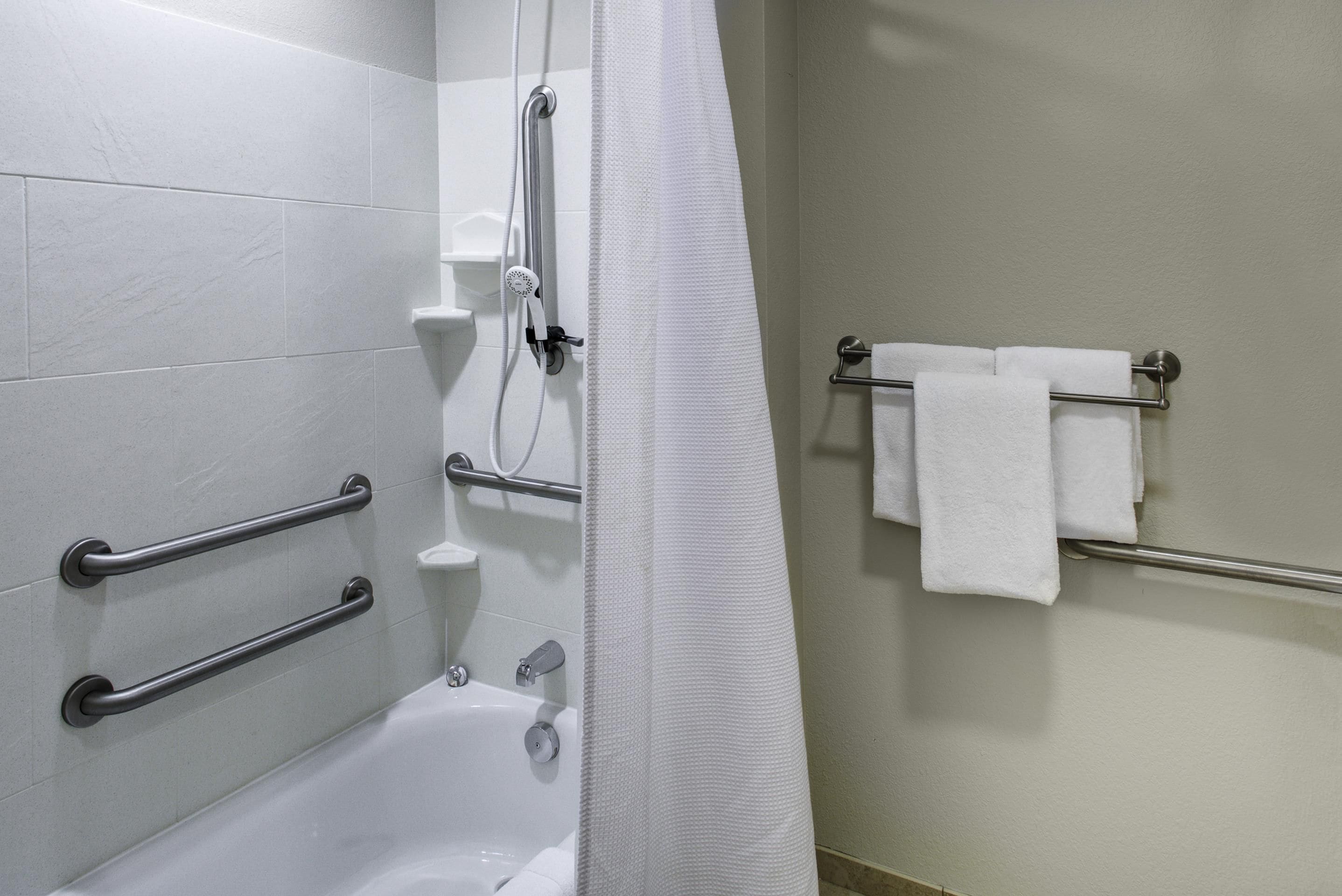 A bathroom with a bathtub, grab bars, a shower head, and a towel rack.