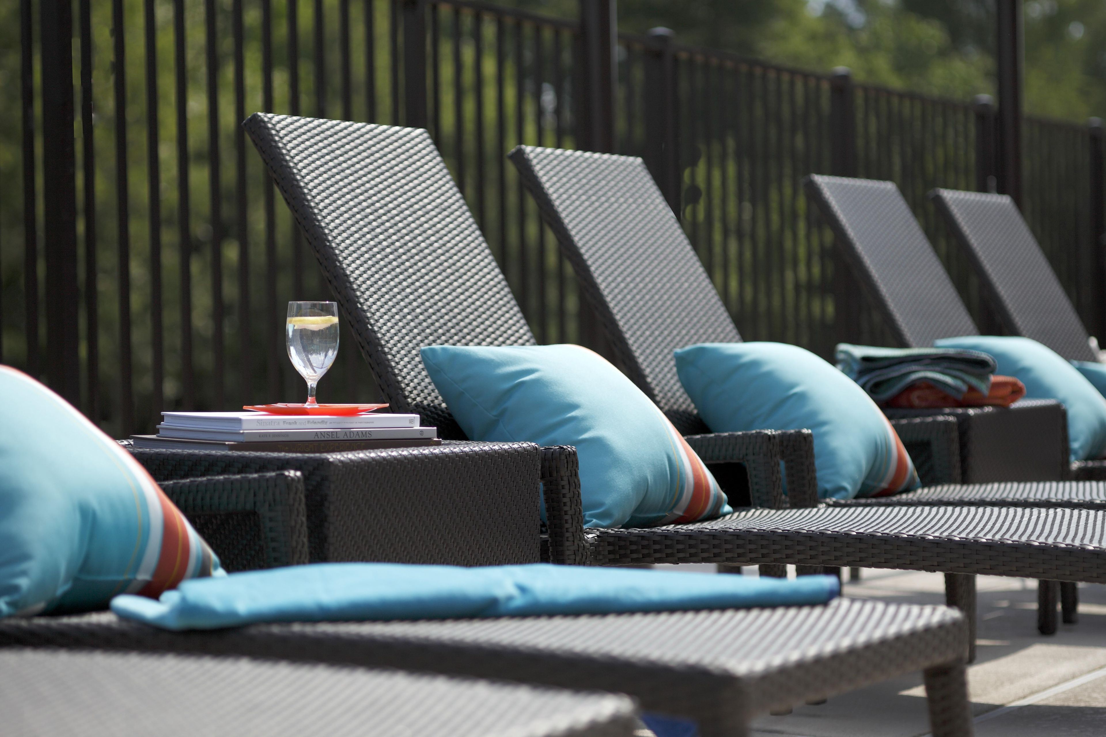 Une rangée de chaises longues avec des coussins, un verre d’eau et un livre sur une table.