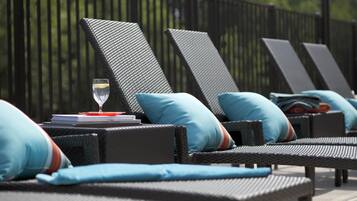 Une rangée de chaises longues avec des coussins, un verre d’eau et un livre sur une table.