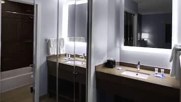 Un baño moderno con cabina de ducha de vidrio, lavamanos con espejo y toallero.