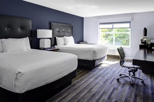 Habitación de hotel con dos camas, un escritorio, una silla y un ventanal grande.