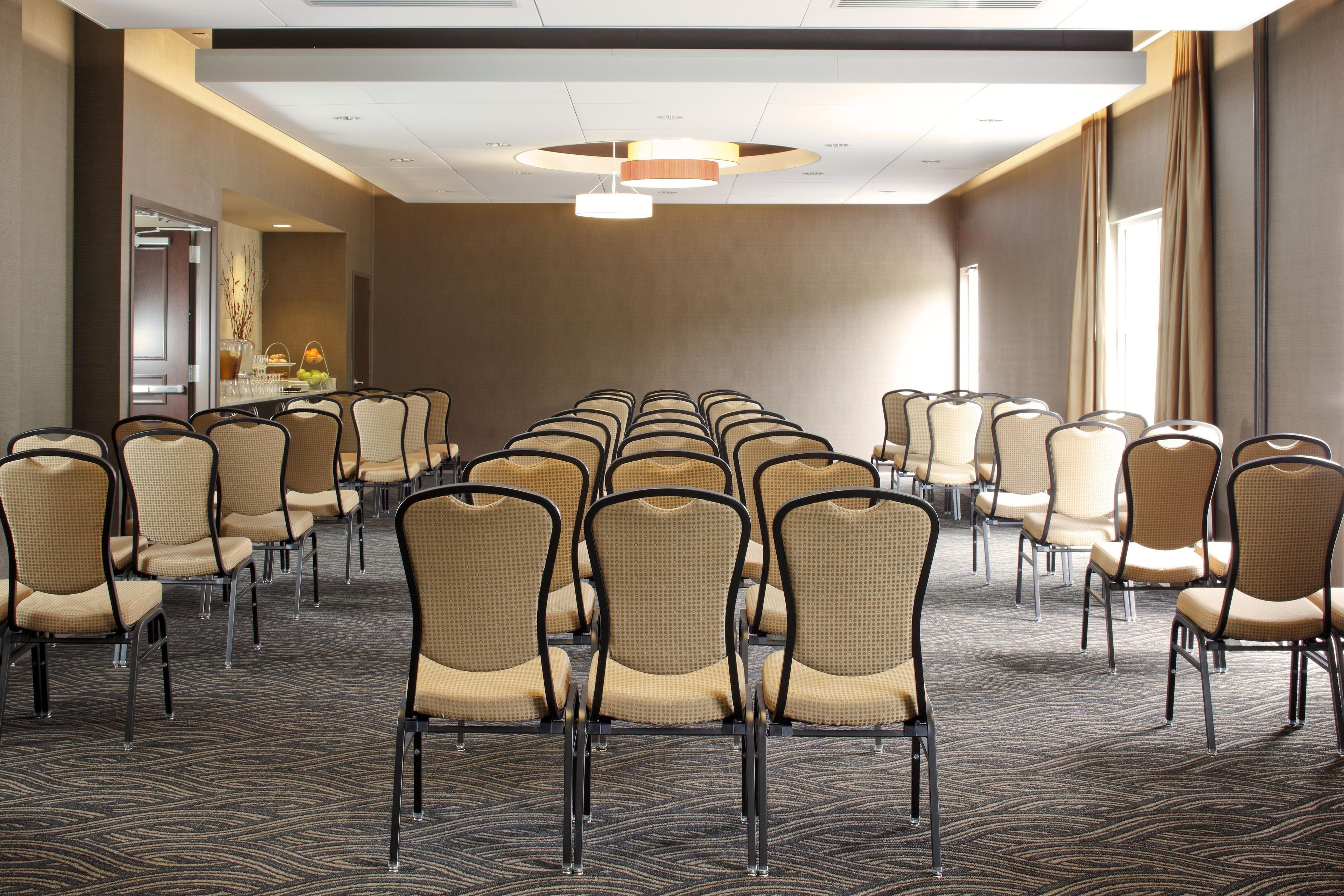 A conference room with rows of chairs, a carpeted floor, and a ceiling light fixture.