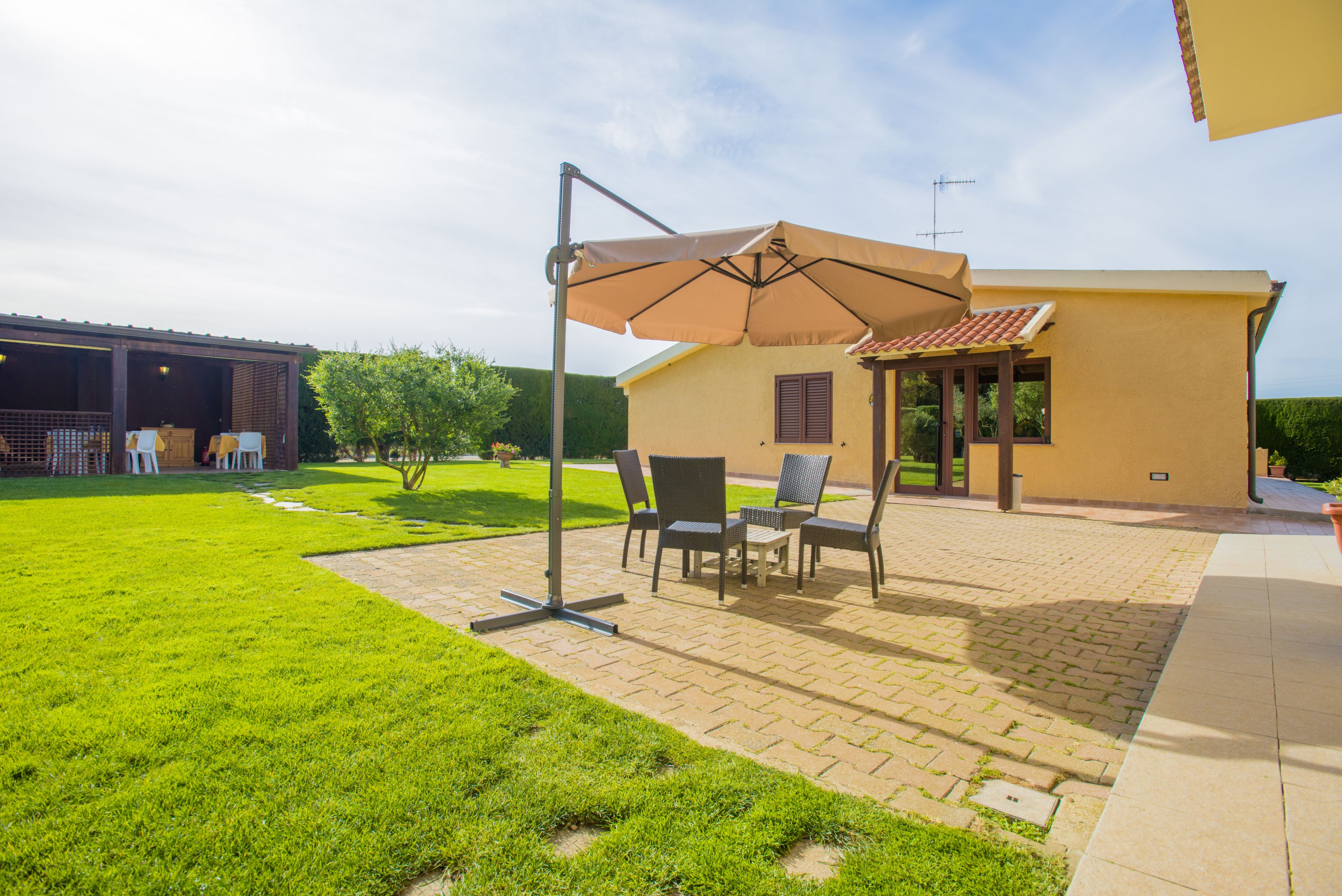 Un patio con mobili da esterno e un ombrellone grande, un edificio con tetto in tegole e un prato curato.