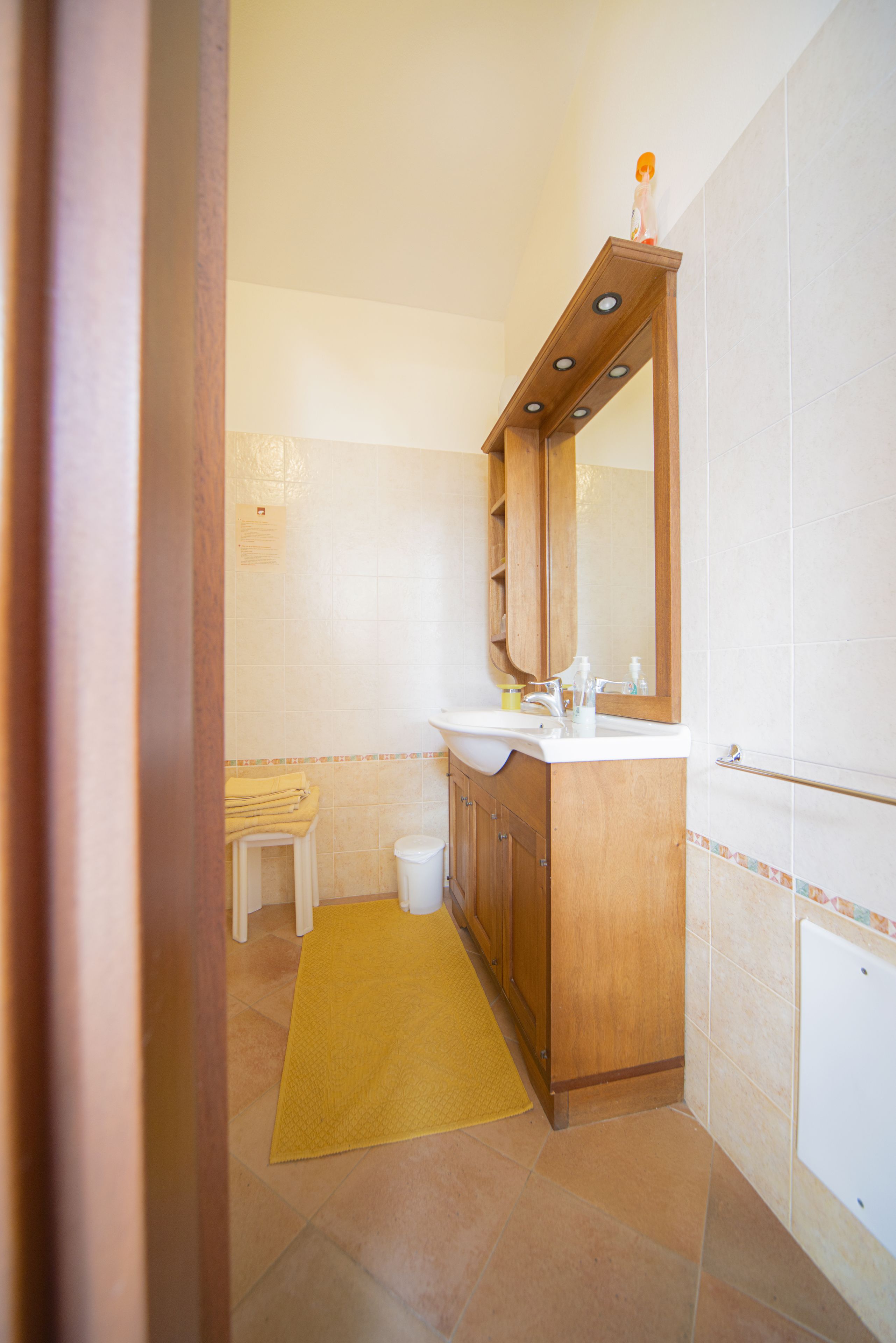 A bathroom with a wooden vanity, a sink, a mirror, and a yellow rug on the floor.