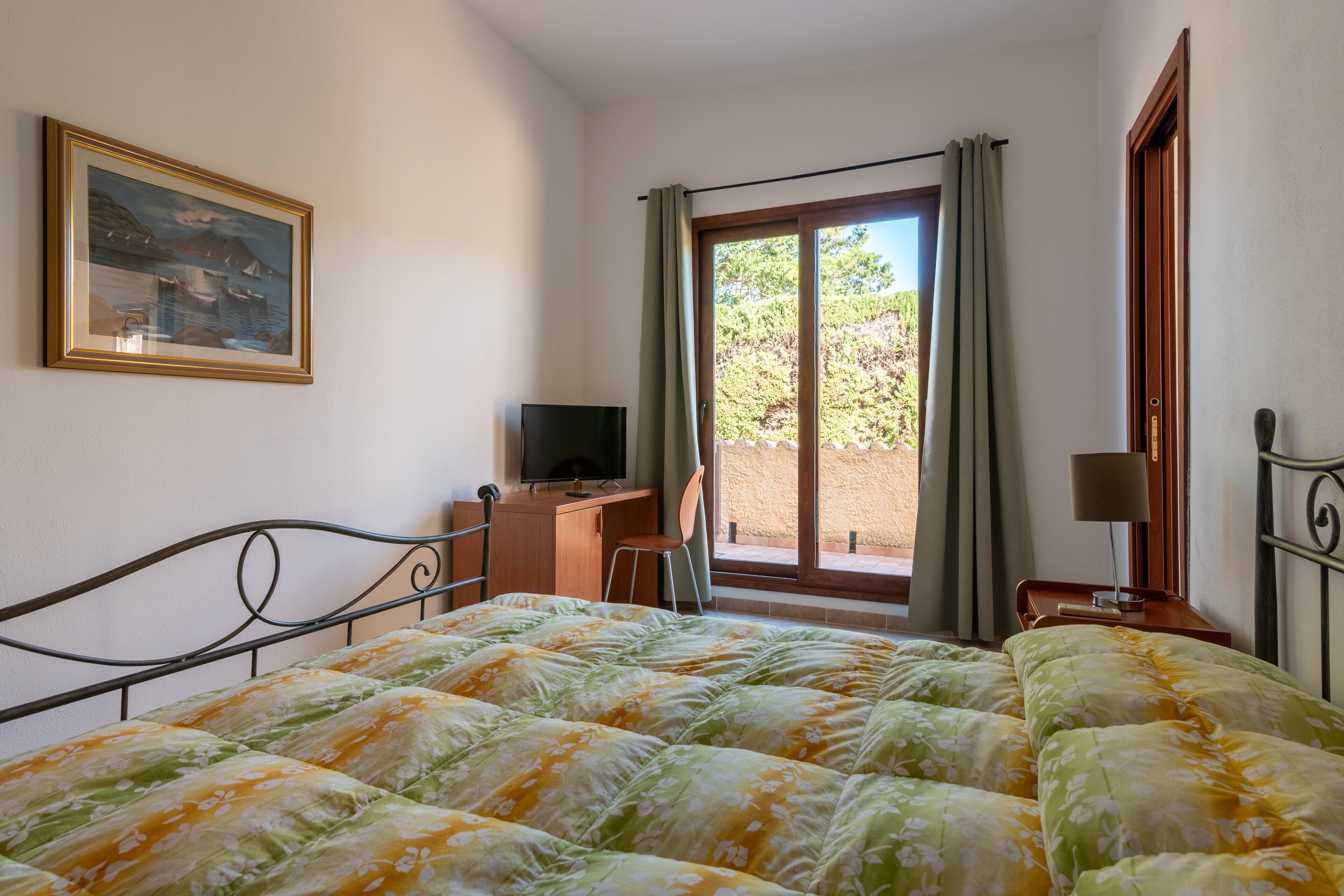 Un dormitorio con cama, escritorio, silla, televisión y ventana con cortinas.