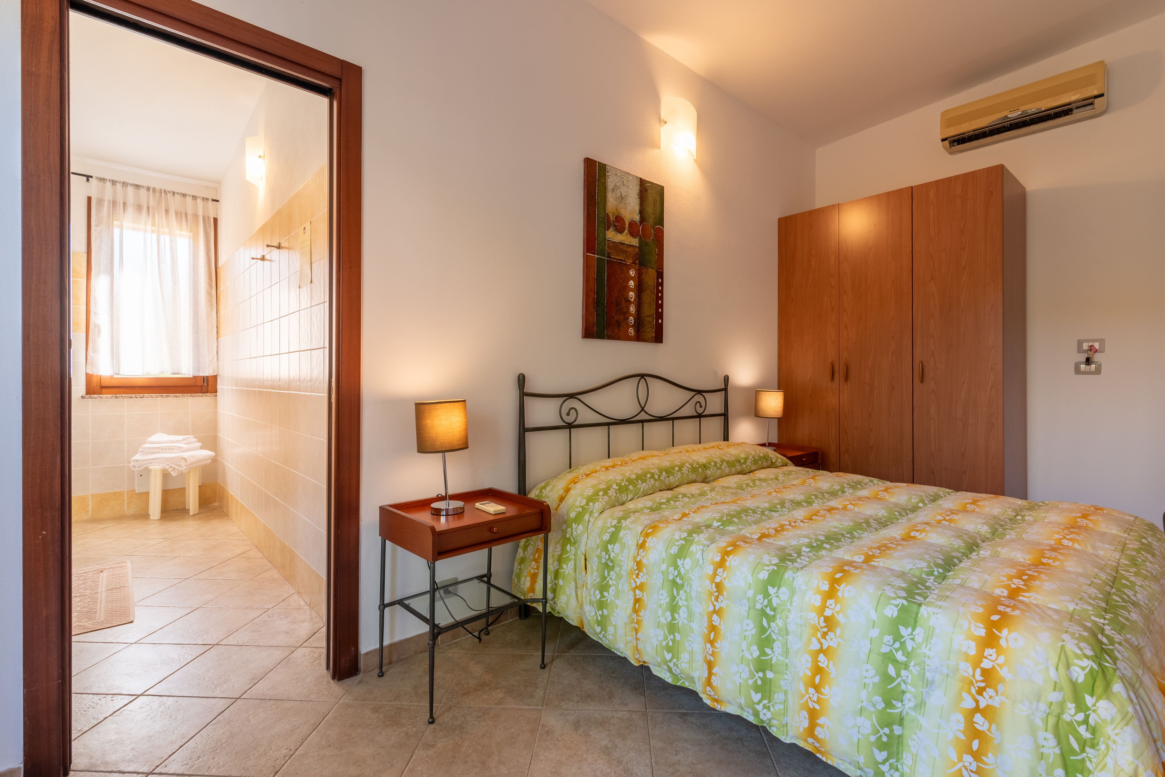 Un dormitorio con cama, lámparas de noche, armario y un cuadro en la pared.