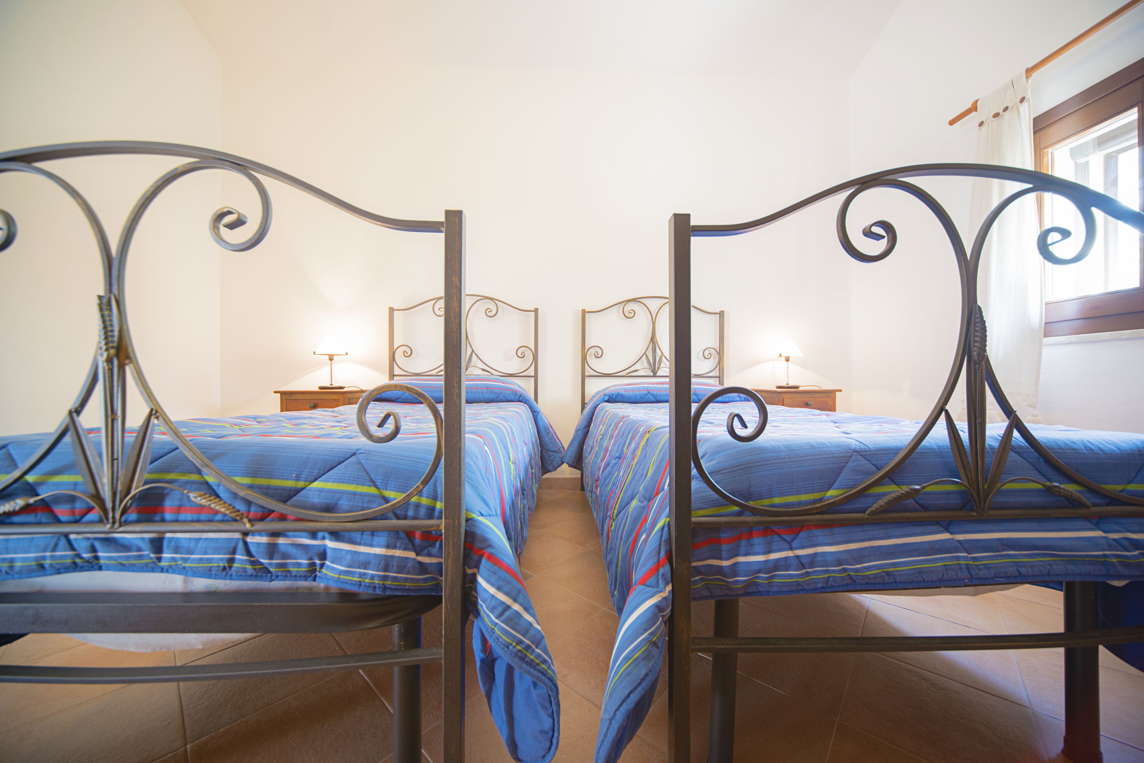 Een kamer met twee bedden, elk met een metalen frame en blauw beddengoed. Er staan nachtkastjes met lampen bij.