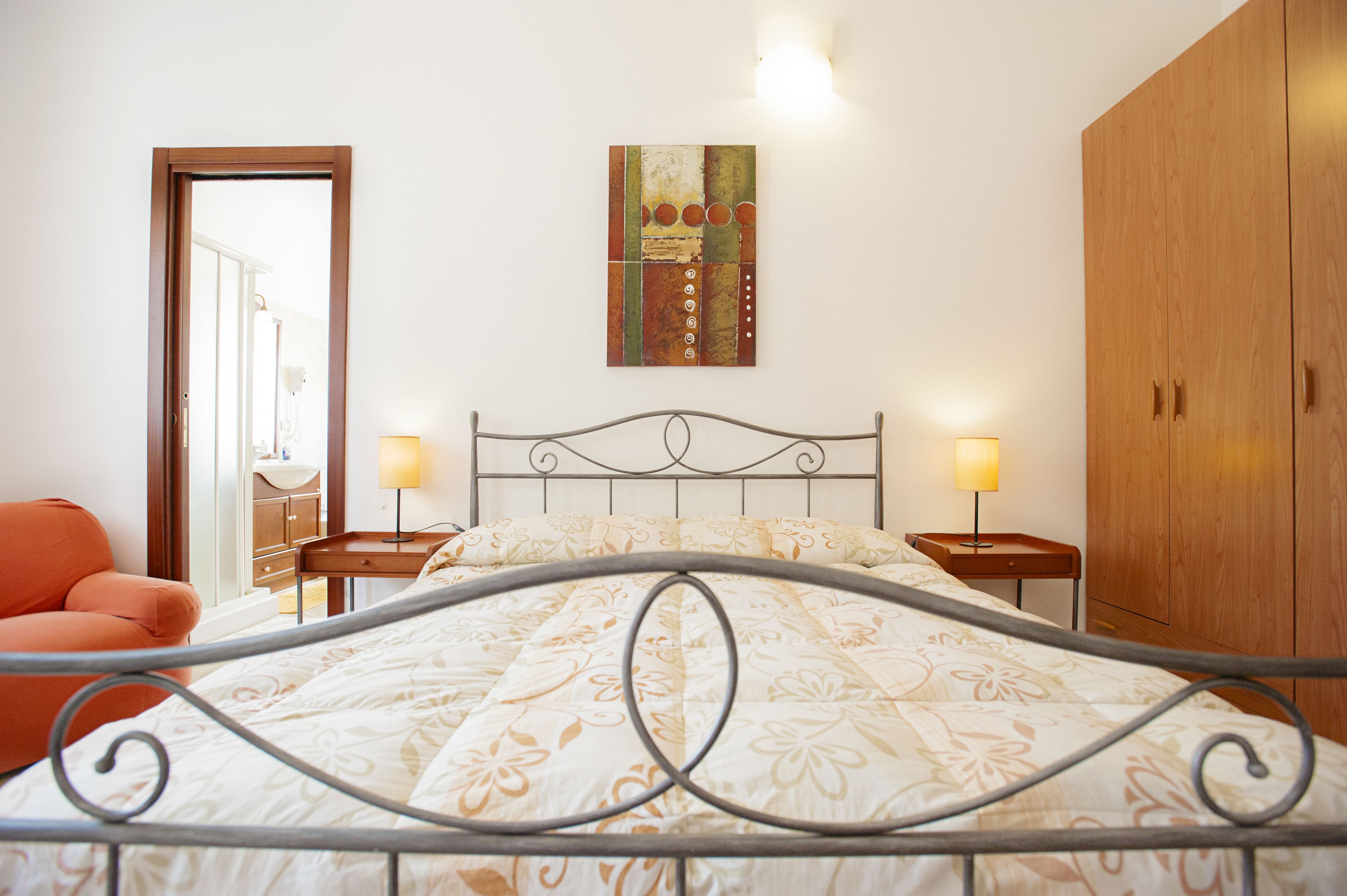 Una camera da letto con un letto, due comodini, una sedia, un armadio e un quadro appeso al muro.