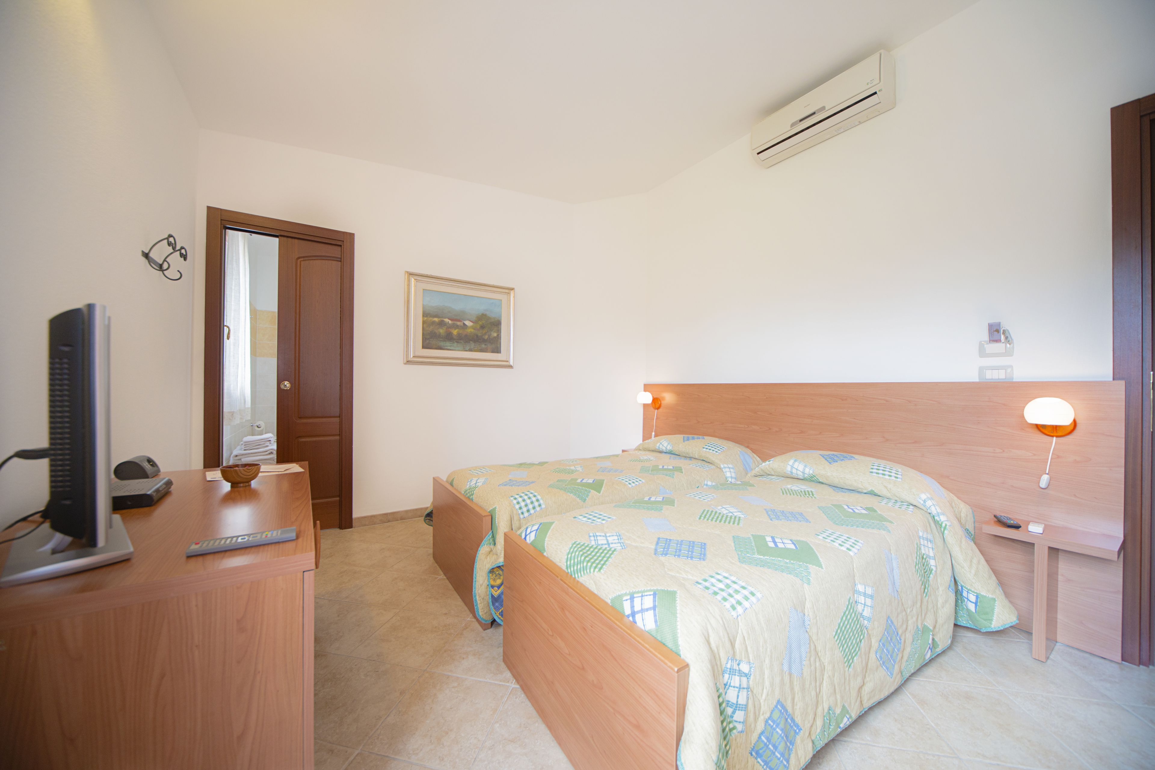 Een slaapkamer met een bed, een bureau, een stoel, een televisie en een airconditioning.