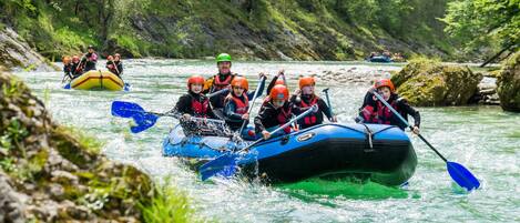 A group of people in a blue inflatable raft navigating a river surrounded by greenery.