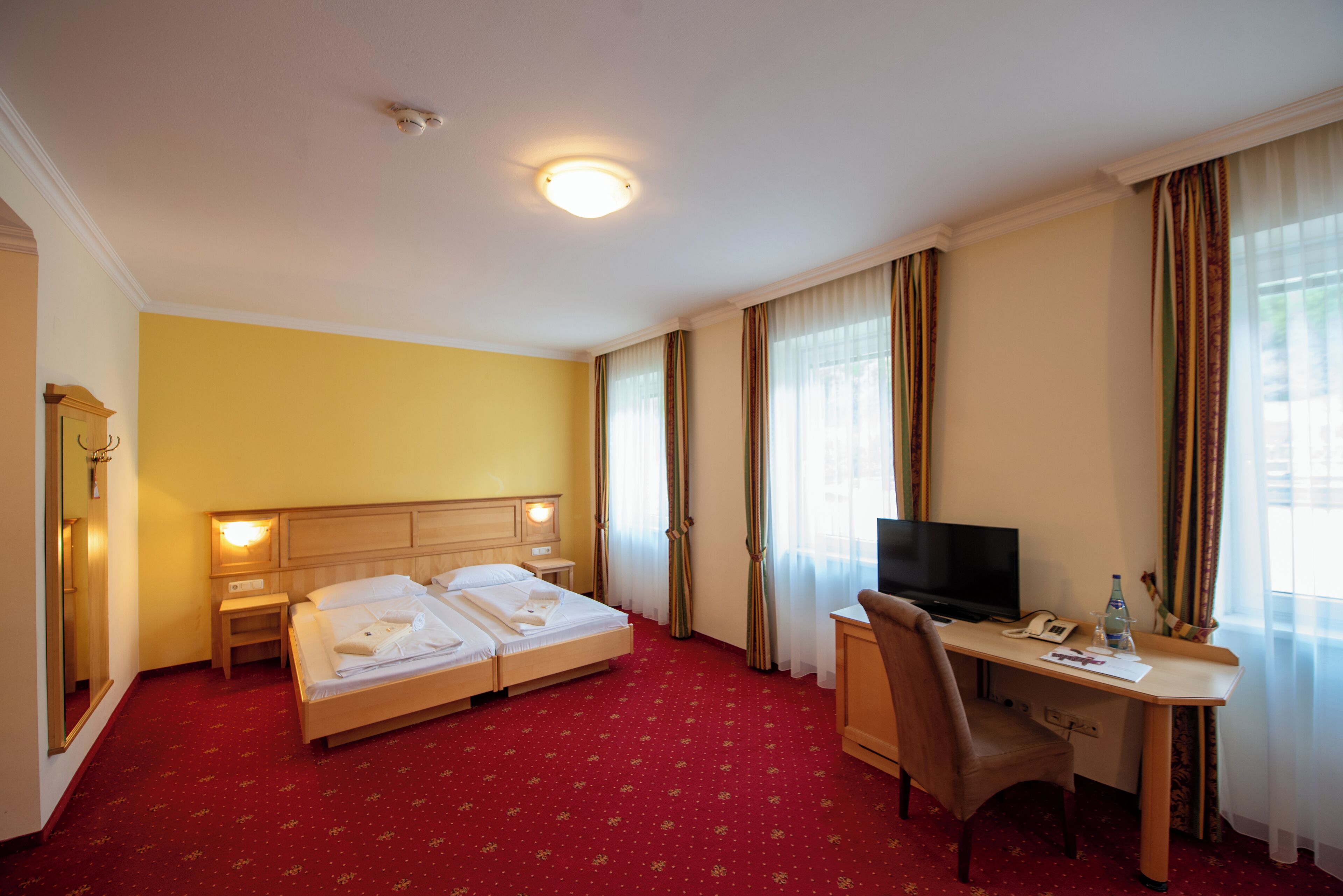 Habitación de hotel con cama doble, escritorio con silla, televisor y lámpara de escritorio.