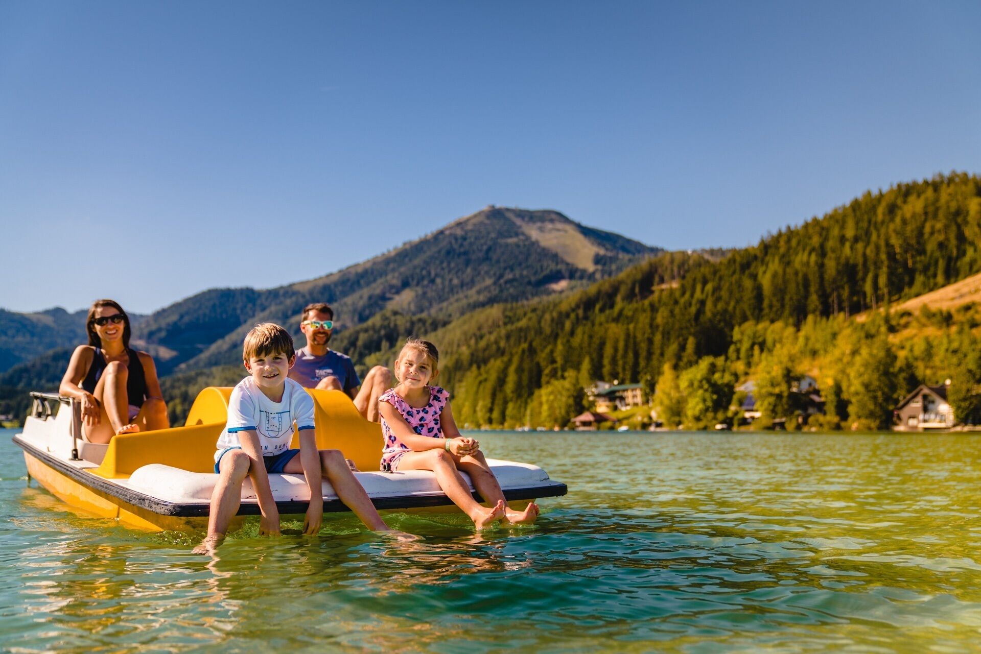 A group of people on a yellow boat with a lake and mountains in the background.