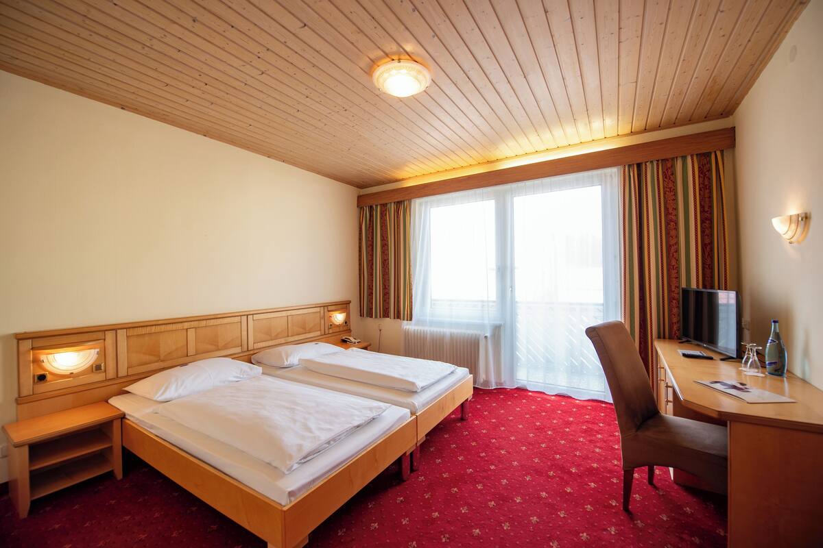 A hotel room with two beds, a desk, a chair, a TV, and a window with curtains.