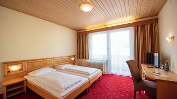 A hotel room with two beds, a desk, a chair, a TV, and a window with curtains.
