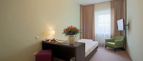 Habitación de hotel con una cama, un escritorio con lámpara, una silla y un televisor montado en la pared.
