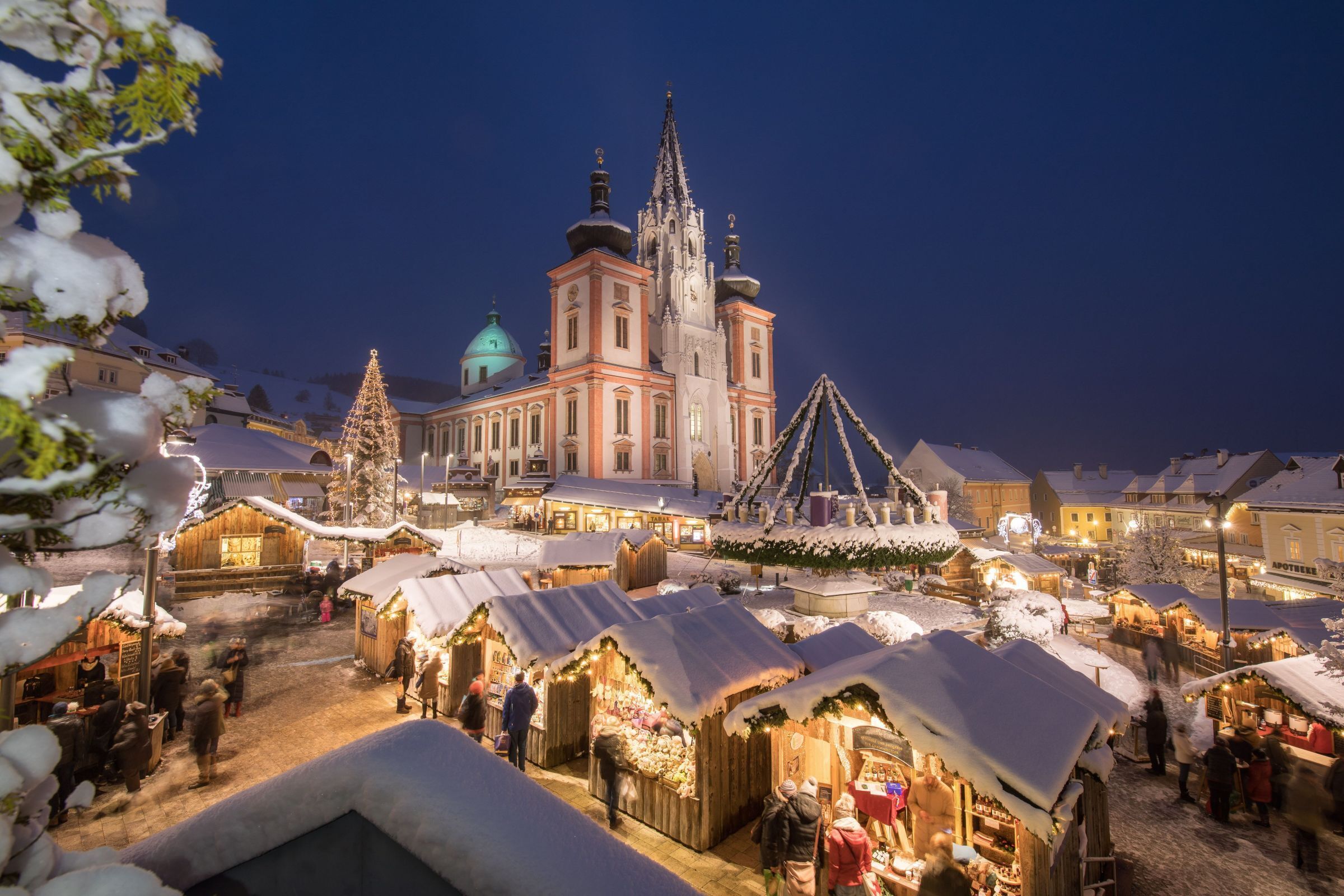 Un mercado al aire libre cubierto de nieve, con edificios tradicionales y una iglesia destacada al fondo.