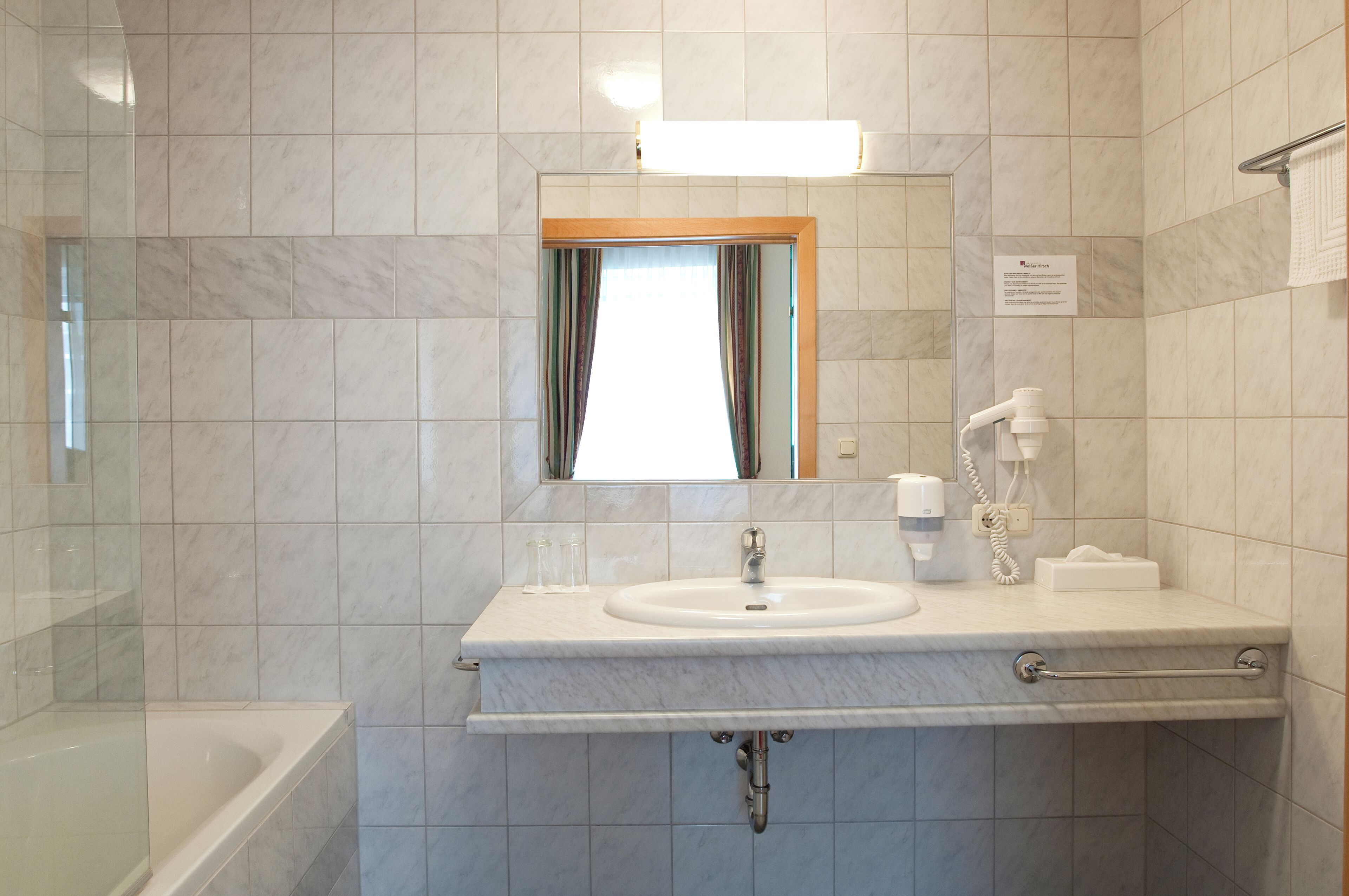 A modern bathroom with a marble sink, a mirror with a wooden frame, a towel rack, and a shower area.