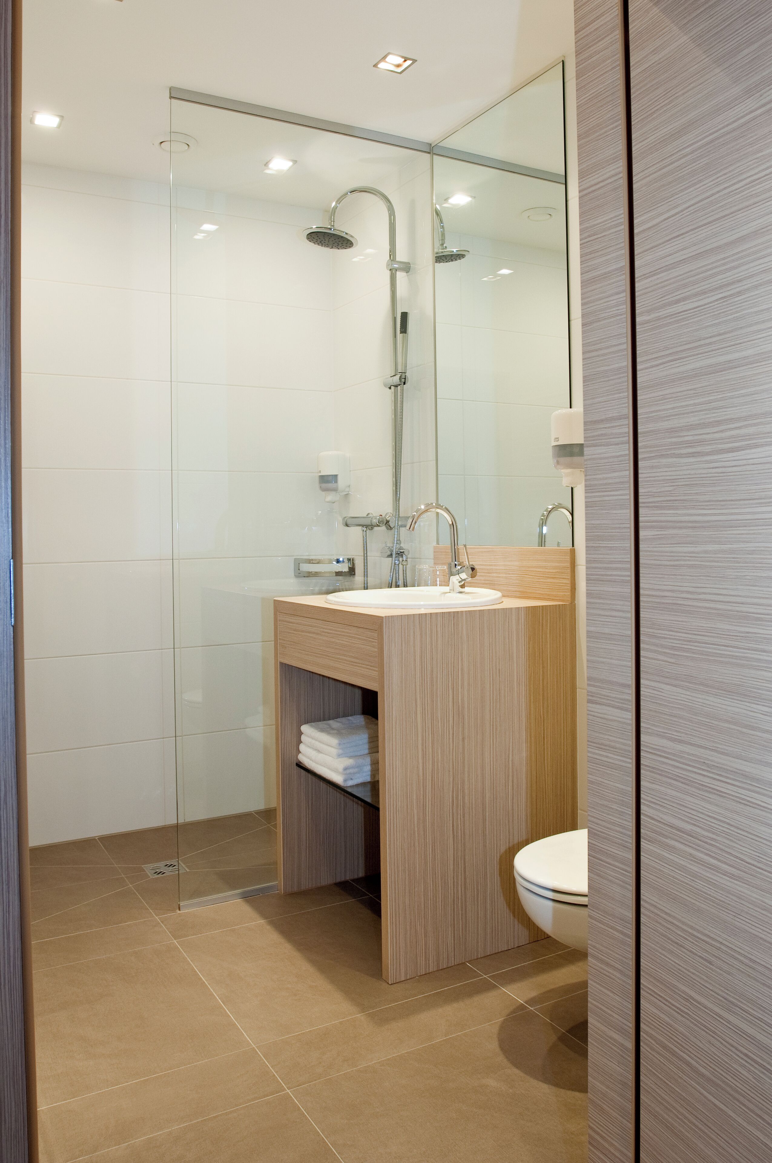 Un baño moderno con cabina de ducha de vidrio, tocador de madera y lavabo blanco.