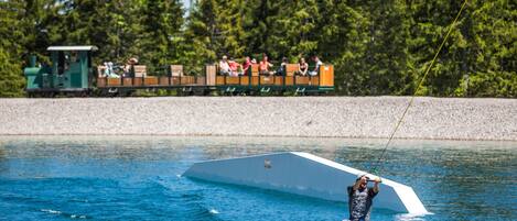 A person wakeboarding on a lake with a train and forest in the background.