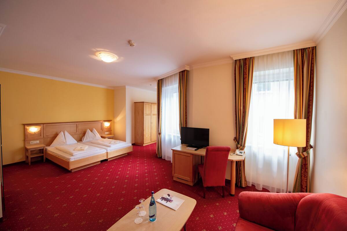 A hotel room with a bed, desk, TV, and red sofa.