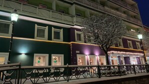 Een hotel met meerdere verdiepingen, balkons, een met sneeuw bedekte boom en verlichte borden.