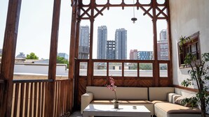 A room with a wooden-framed window, a beige sofa, a small table with a potted plant, and a view of tall buildings. - Happy House Hostel (Santiago)