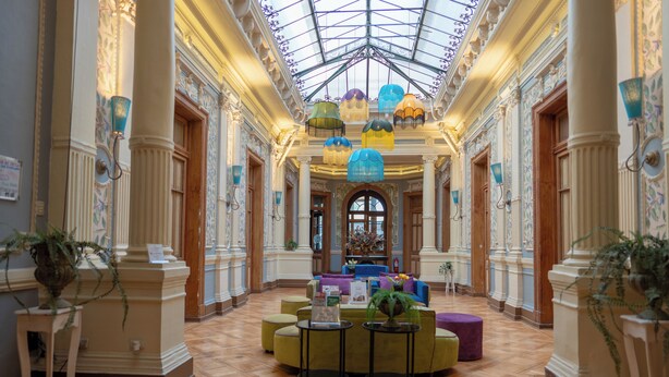 A spacious lobby with a high ceiling, ornate columns, and a central seating area with colorful sofas and tables. - Happy House Hostel (Santiago)