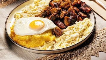 A plate of food with a fried egg, hash browns, and sausage on a table with a lace tablecloth.