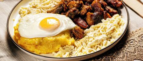 A plate of food with a fried egg, hash browns, and sausage on a table with a lace tablecloth.