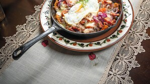 Una mesa de madera con mantel de encaje, una olla con comida, un bol de verduras, una copa de vino y un barril de madera.