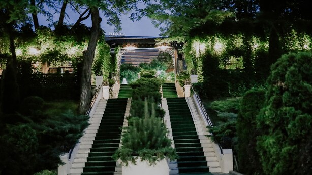 Entrada de hotel con una escalera que sube a un área cubierta, rodeada de vegetación.