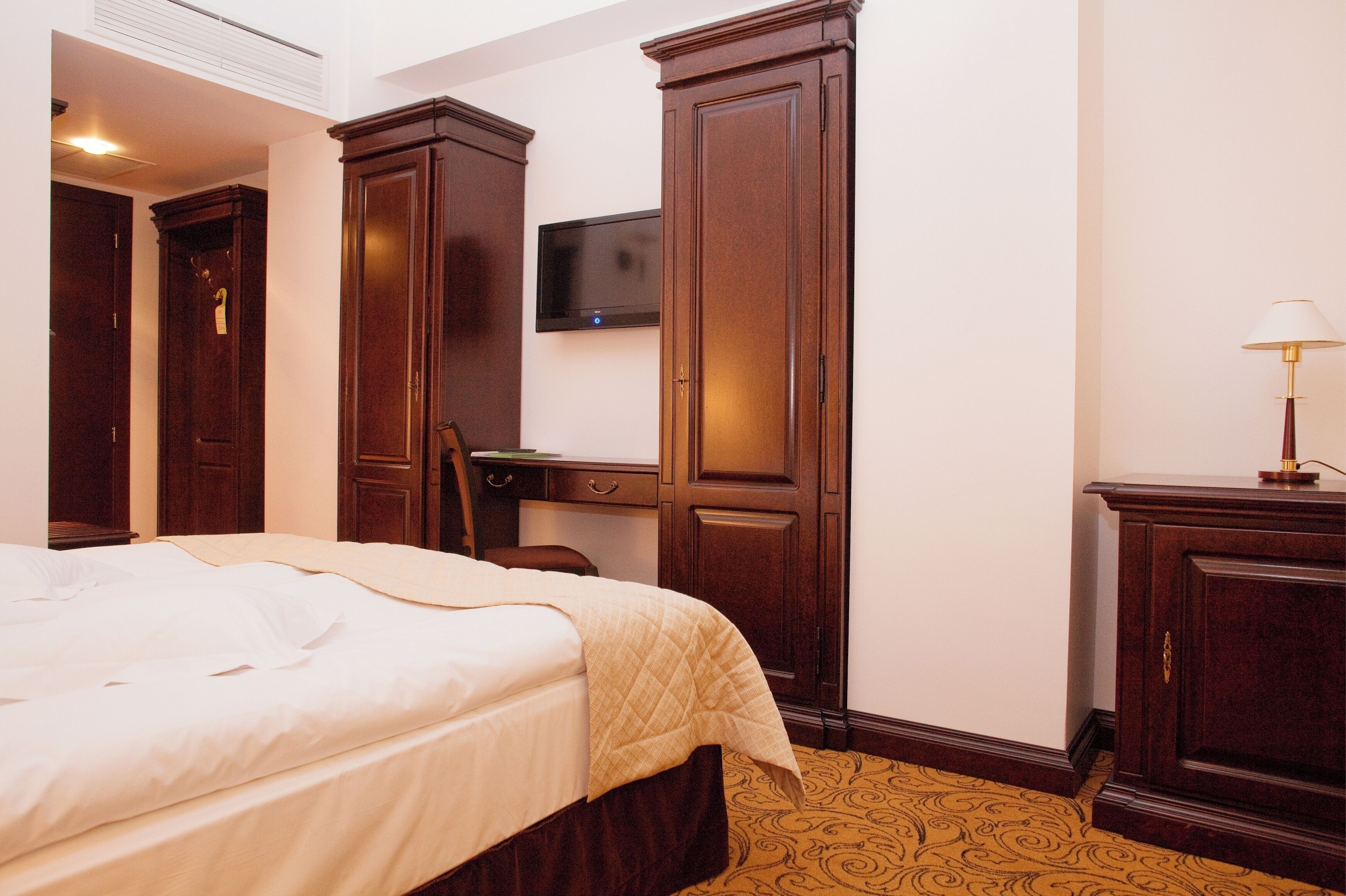A hotel room with a bed, a desk, a television, and a lamp.