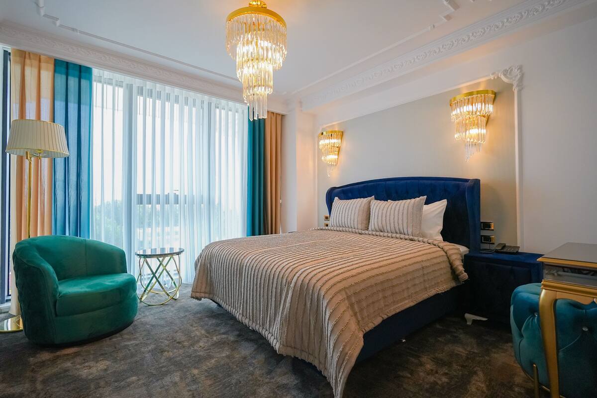 Habitación de hotel con una cama grande, un sillón verde, una mesita redonda y dos lámparas fijadas a la pared.