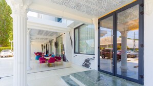 A modern hotel entrance with a glass door, white columns, and a seating area with colorful chairs. - W Regal Boutique&Spa (Constanta)