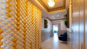 A hallway with a patterned wall, a chandelier, and a blue chair. - W Regal Boutique&Spa (Constanta)