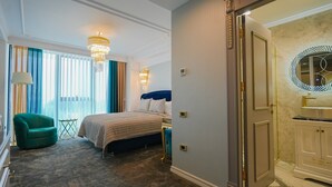 A hotel room with a bed, a green armchair, a chandelier, and a bathroom with a marble floor and a mirror. - W Regal Boutique&Spa (Constanta)