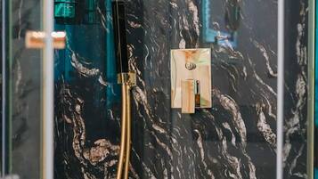Casa de banho com parede de mármore preto, um chuveiro dourado e cabine de chuveiro em vidro.