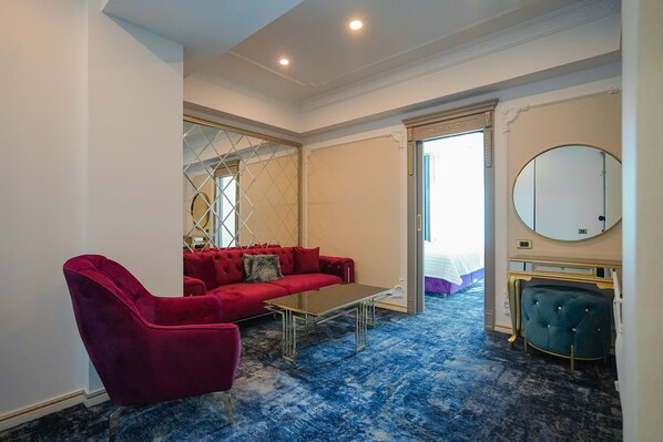 A hotel room with a red sofa, a glass coffee table, a round mirror, and a blue carpet. - W Regal Boutique&Spa (Constanta)