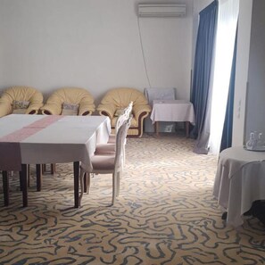 Habitación de hotel con una mesa de comedor, dos sillones amarillos, una mesita con una silla, alfombra estampada y un equipo de aire acondicionado.